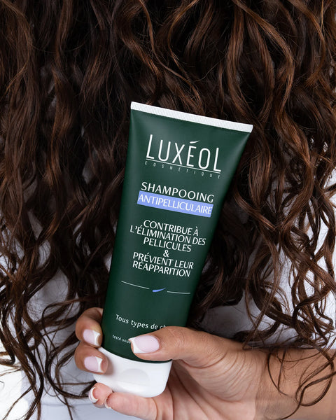 Hand holding a Luxéol shampoo tube with curly hair in the background