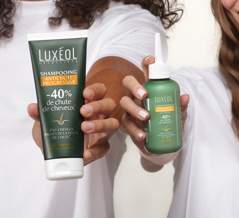 Two hands holding Luxéol shampoo and conditioner bottles against a white background