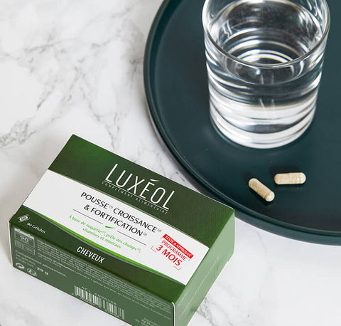 Luxéol hair growth and strengthening supplement packaging with capsules and a glass of water on a marble surface.