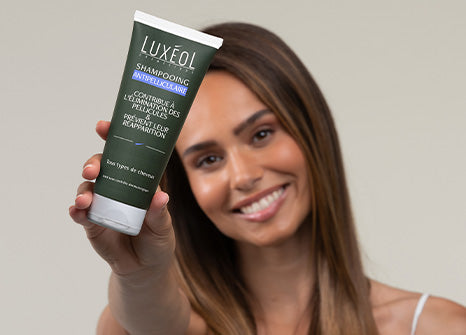 Tube of dark green Luxéol anti dandrug shampoo on white background with women holding