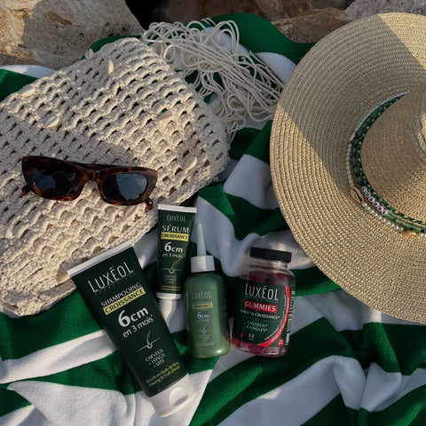 Luxueol skincare products with a sun hat and sunglasses on a beach towel