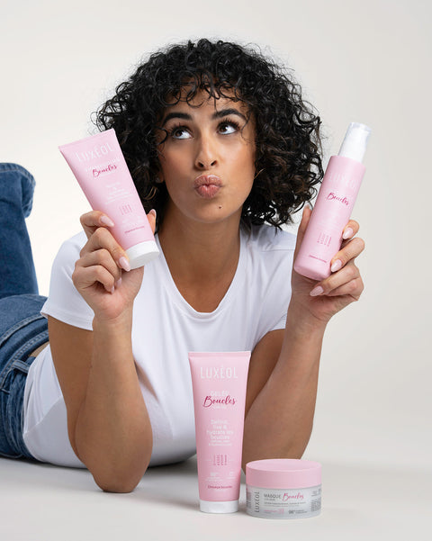 Naine hoiab roosa juuksehooldustoodete komplekti neutraalses taustas