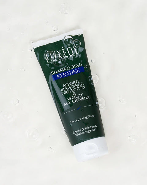 Tube of Luxeol Keratin Shampoo on a white background with water droplets.