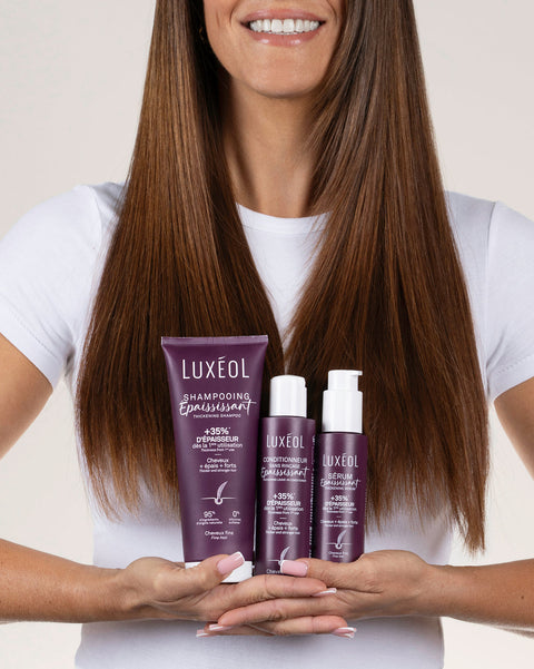 Moteris laiko Luxéol plaukų priežiūros priemones paprastame fone.