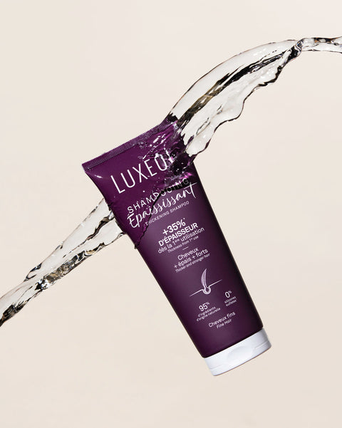 Violetinė Luxéol plaukų priežiūros priemonė su vandens purslais smėlio spalvos fone
