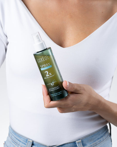 Person holding a Luxe Oil spray bottle against a white background