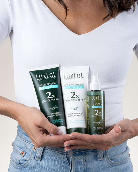 Person holding Luxéol hair care products including shampoo, conditioner, and spray.